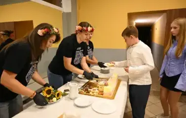 widzimy panią krojącą tort oraz osoby czekające na tort 