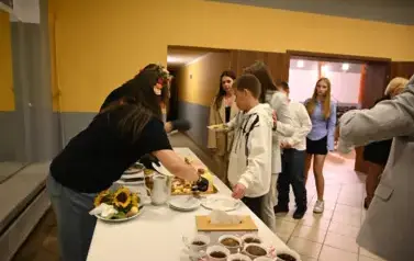 widzimy panią krojącą tort oraz osoby czekające na tort 
