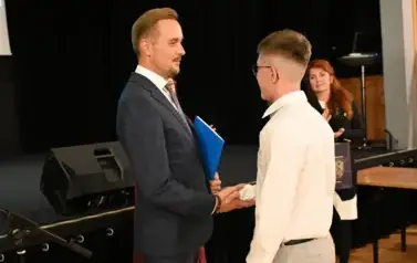 widzimy pana Burmistrza podającego dłoń chłopcu by mu pogratulować oraz wreczyc stypendium i upominek