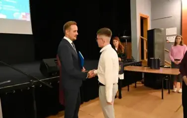 widzimy pana Burmistrza podającego dłoń chłopcu by mu pogratulować oraz wreczyc stypendium i upominek