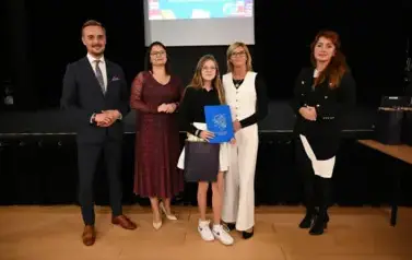 widzimy 3 panie, pana oraz dziewczynkę, kt&oacute;ra otrzymała stypendium i upominek