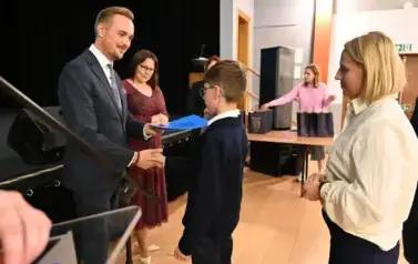 widzimy pana Burmistrza podającego dłoń chłopcu by mu pogratulować oraz wreczyc stypendium i upominek