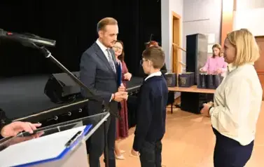 widzimy pana Burmistrza podającego dłoń chłopcu by mu pogratulować oraz wreczyc stypendium i upominek