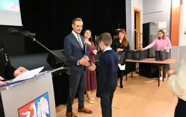 widzimy pana Burmistrza podającego dłoń chłopcu by mu pogratulować oraz wreczyc stypendium i upominek