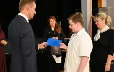 widzimy pana Burmistrza podającego dłoń chłopcu by mu pogratulować oraz wreczyc stypendium i upominek