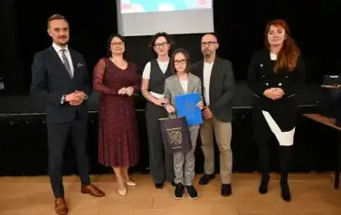 widzimy 3 panie, 2 pan&oacute;w oraz dziecko, kt&oacute;re otrzymało stypendium oraz upominek