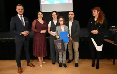 widzimy 3 panie, 2 pan&oacute;w oraz dziecko, kt&oacute;re otrzymało stypendium oraz upominek
