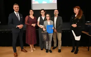 widzimy 3 panie, 2 pan&oacute;w oraz dziecko, kt&oacute;re otrzymało stypendium oraz upominek