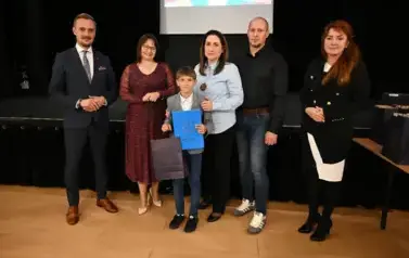 widzimy 3 panie, 2 pan&oacute;w oraz chłopca, kt&oacute;ry otrzymał stypendium oraz podarunek