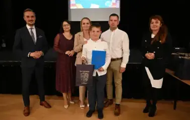 widzimy 3 panie, 2 pan&oacute;w oraz chłopca trzymającego stypendium oraz upominek