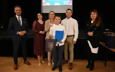 widzimy 3 panie, 2 pan&oacute;w oraz chłopca trzymającego stypendium oraz upominek