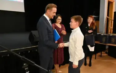 widzimy pana Burmistrza podającego dłoń chłopcu by mu pogratulować oraz wreczyc stypendium i upominek