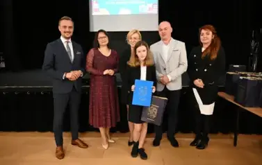 widzimy 3 panie, 2 pan&oacute;w oraz dziewczynke, kt&oacute;ra otrzymała stypendium oraz upominek