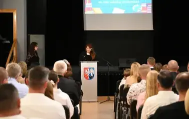 widzimy siedzącą publiczność oraz m&oacute;wiącą panią do mikrofonu