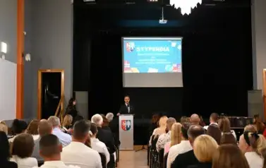 widzimy siedzącą publiczność oraz pana Burmistrza m&oacute;wiącego do mikrofonu