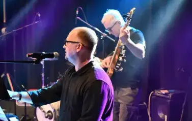 widzimy pana grającego na gitarze oraz pana siedzącego przy mikrofonie
