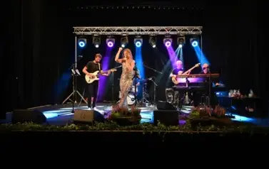 widzimy panią, kt&oacute;ra śpiewa do mikrofonu oraz pan&oacute;w grających na instrumentach