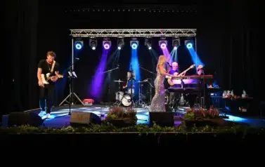 widzimy panią, kt&oacute;ra śpiewa do mikrofonu oraz pan&oacute;w grających na instrumentach