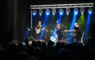widzimy panią śpiewającą na scenie oraz pan&oacute;w grających na instrumentach