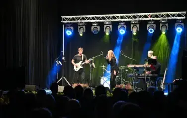 widzimy panią śpiewającą na scenie oraz pan&oacute;w grających na instrumentach