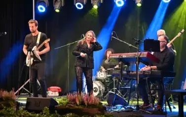 widzimy panią tańczącąna na scenie oraz pan&oacute;w grających na instrumentach
