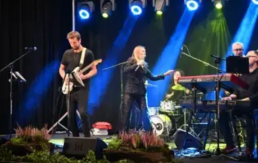 widzimy panią tańczącąna na scenie oraz pan&oacute;w grających na instrumentach