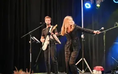 widzimy panią trzymającą mikrofon w ręce oraz pana grającego na gitarze