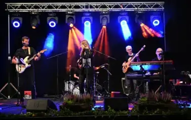 widzimy panią śpiewającą do mikrofonu oraz pan&oacute;w grających na instrumentach