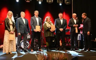 widzimy grupe os&oacute;b stojącą na scenie z podarunkami w ręce