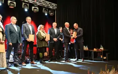 widzimy grupe stojącą z podarunkami w rękach oraz pana przekazującego dalsze upominki