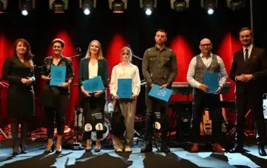 widzimy grupe os&oacute;b stojącą na scenie z podarunkami w ręce