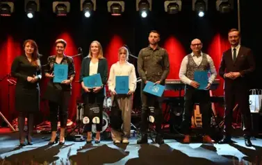 widzimy grupe os&oacute;b stojącą na scenie z podarunkami w ręce