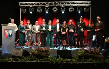 widzimy grupe os&oacute;b stojącą na scenie z podarunkami w ręce