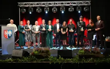 widzimy grupe os&oacute;b stojącą na scenie z podarunkami w ręce