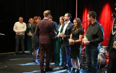 widzimy pana oraz panią podających podarunek grukie os&oacute;b stojących w rzędzie na scenie