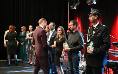 widzimy pana podającego podarunek grukie os&oacute;b stojących w rzędzie na scenie