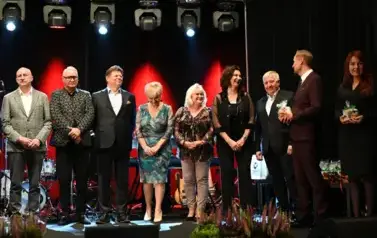 widzimy 4 panie oraz 5 pan&oacute;w stojących na scenie