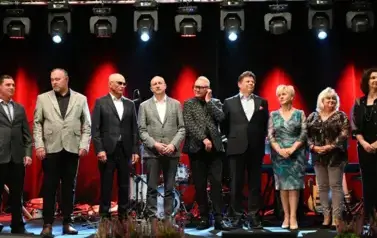 widzimy 3 panie oraz 6 pan&oacute;w stojących na scenie
