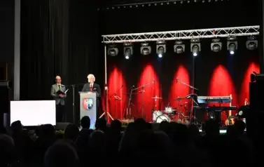 widzimy scene oraz pana m&oacute;wiącego do mikrofonu oraz pana stojącego w tle