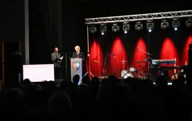widzimy scene oraz pana m&oacute;wiącego do mikrofonu oraz pana stojącego w tle
