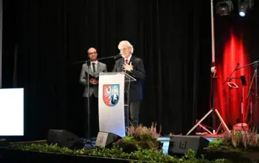 widzimy pana m&oacute;wiącego do mikrofonu oraz pana stojącego w tle