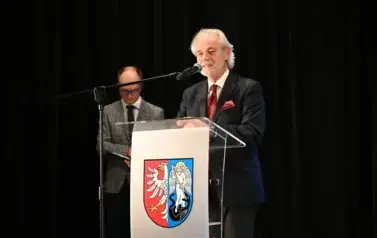 widzimy pana m&oacute;wiącego do mikrofonu oraz pana stojącego w tle