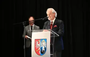widzimy pana m&oacute;wiącego do mikrofonu oraz pana stojącego w tle