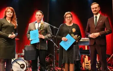widzimy 2 panie i 2 pan&oacute;w, jedna pani oraz pan trzymają prezent oraz r&oacute;że w rękach