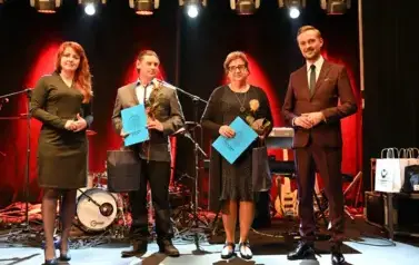 widzimy 2 panie i 2 pan&oacute;w, jedna pani oraz pan trzymają prezent oraz r&oacute;że w rękach