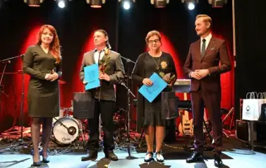 widzimy 2 panie i 2 pan&oacute;w, jedna pani oraz pan trzymają prezent oraz r&oacute;że w rękach