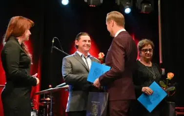 widzimy dw&oacute;ch pan&oacute;w,jednen z nich gratuluje innemu panu oraz trzyma podarunek w rękach