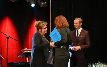 widzimy dwie pani, jedna z nich gratuluje drugiej pani oraz trzyma w rękach nagrode