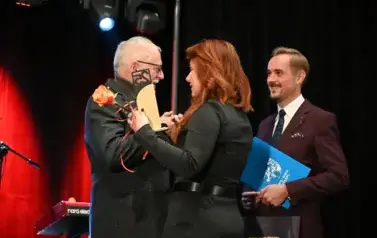 widzimy panią przekazującą r&oacute;że oraz statuetke panu