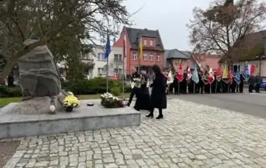 widzimy grupe ze sztandarmi oraz grupe innych os&oacute;b podchodzących do pomnika